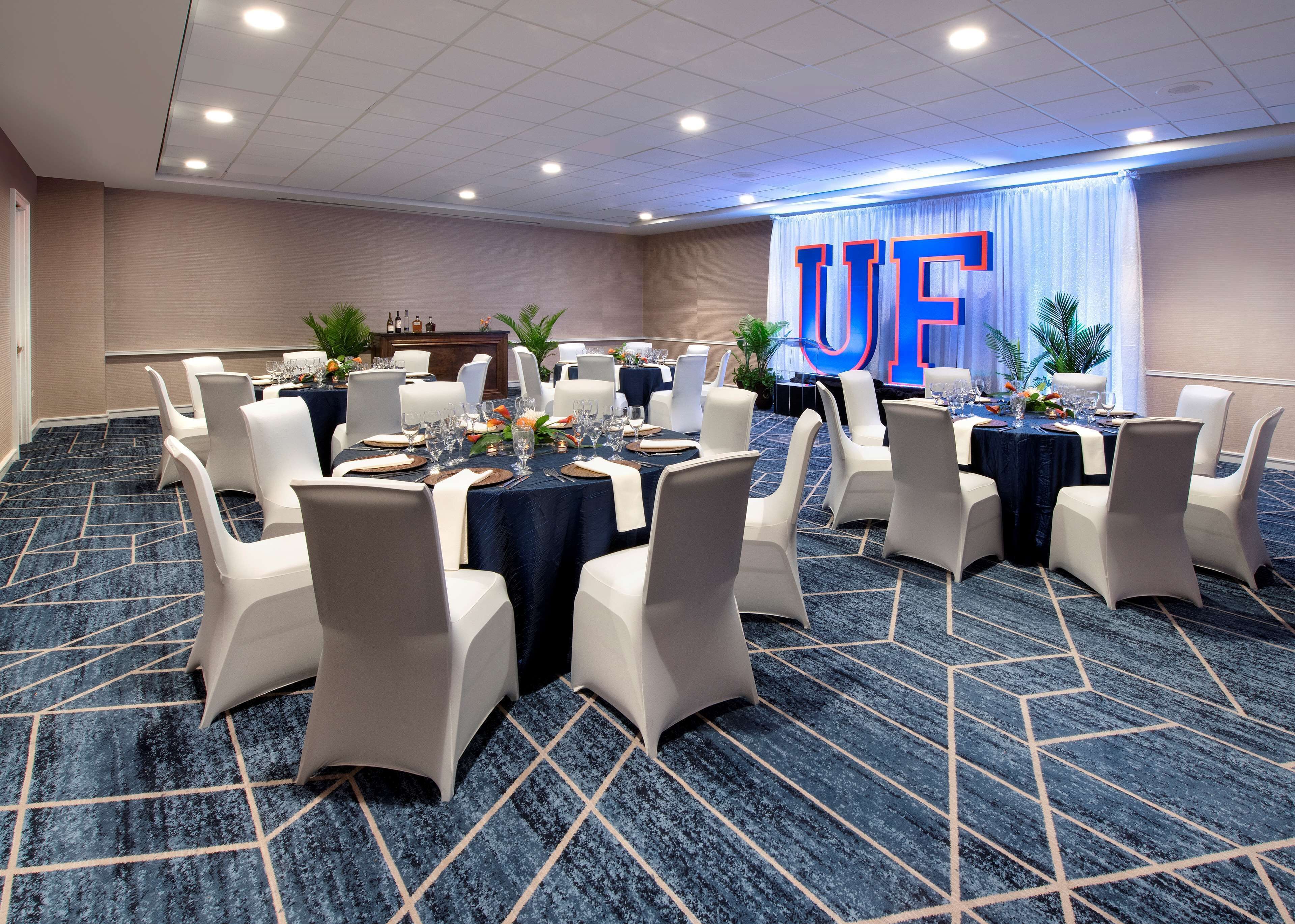 Une salle de conférence avec des tables rondes, des chaises blanches et un grand panneau « UF » sur le mur.
