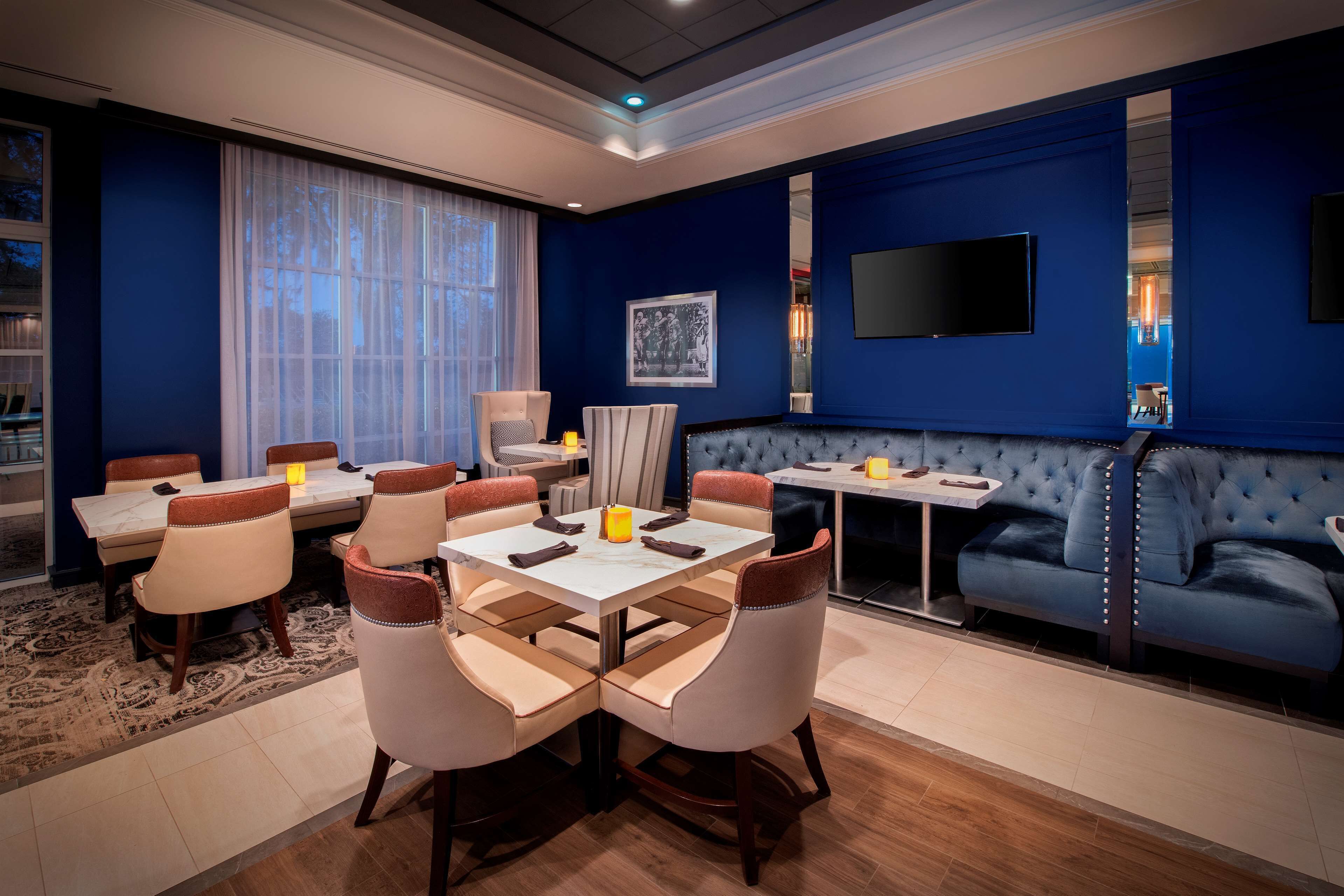 A modern hotel room with a dining area, a sofa, and a flat-screen TV.