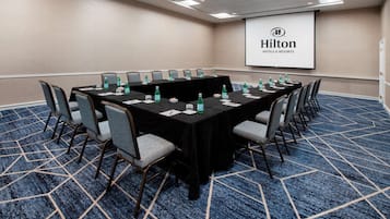 Une salle de conférence avec une longue table, des chaises et un écran de projection affichant le logo de Hilton.