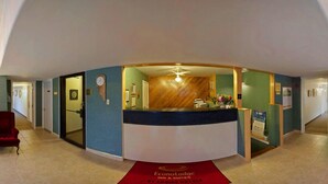 Zona de recepción con mostrador curvo, un reloj y alfombra roja con el nombre del hotel.