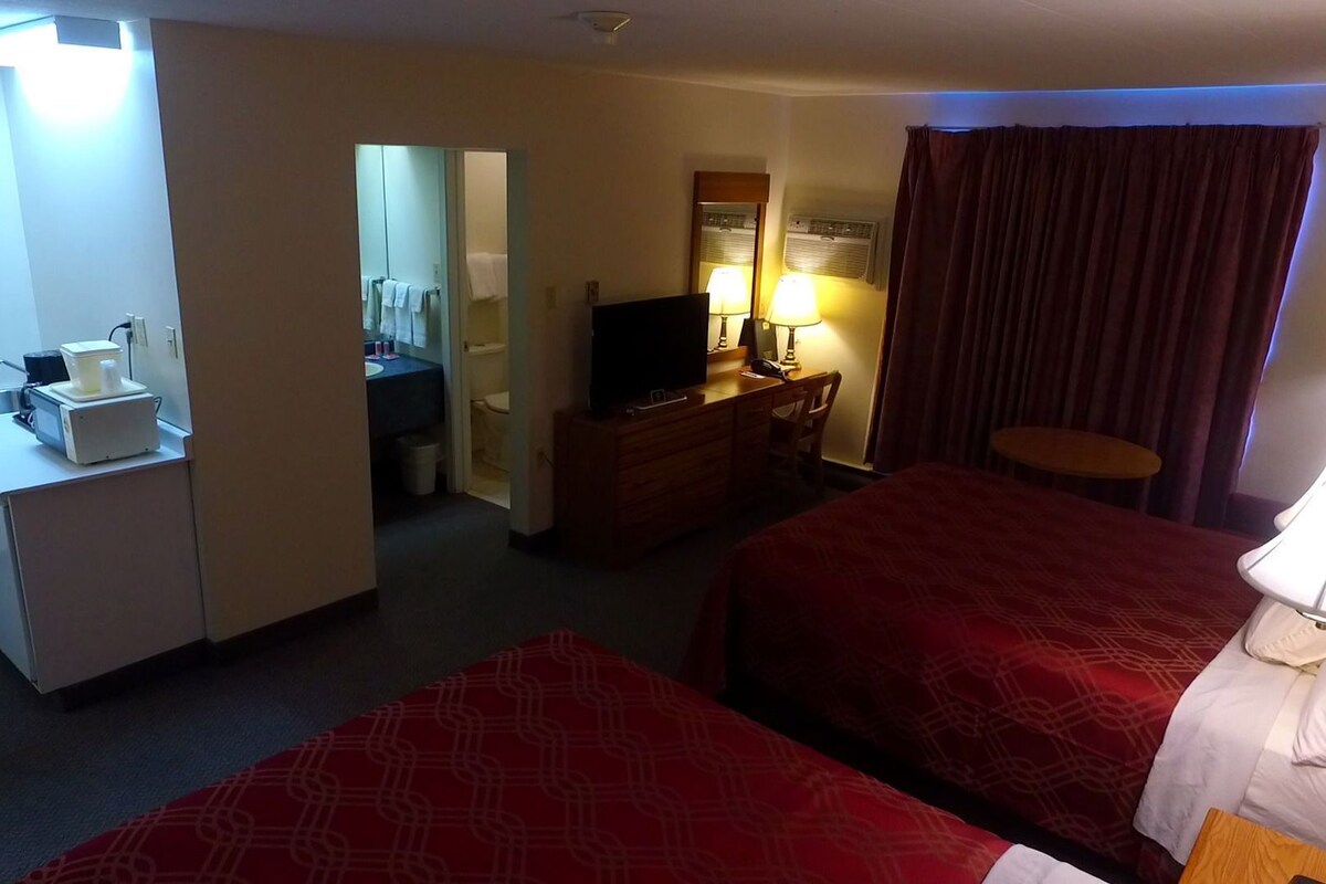 Une chambre d’hôtel équipée d’un bureau, d’une télévision, d’un lit, d’une petite table et d’une lampe.