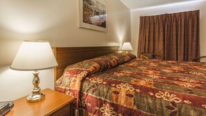 Una habitación de hotel con una cama bien hecha, una lámpara de noche, un cuadro en la pared y una ventana con cortinas.