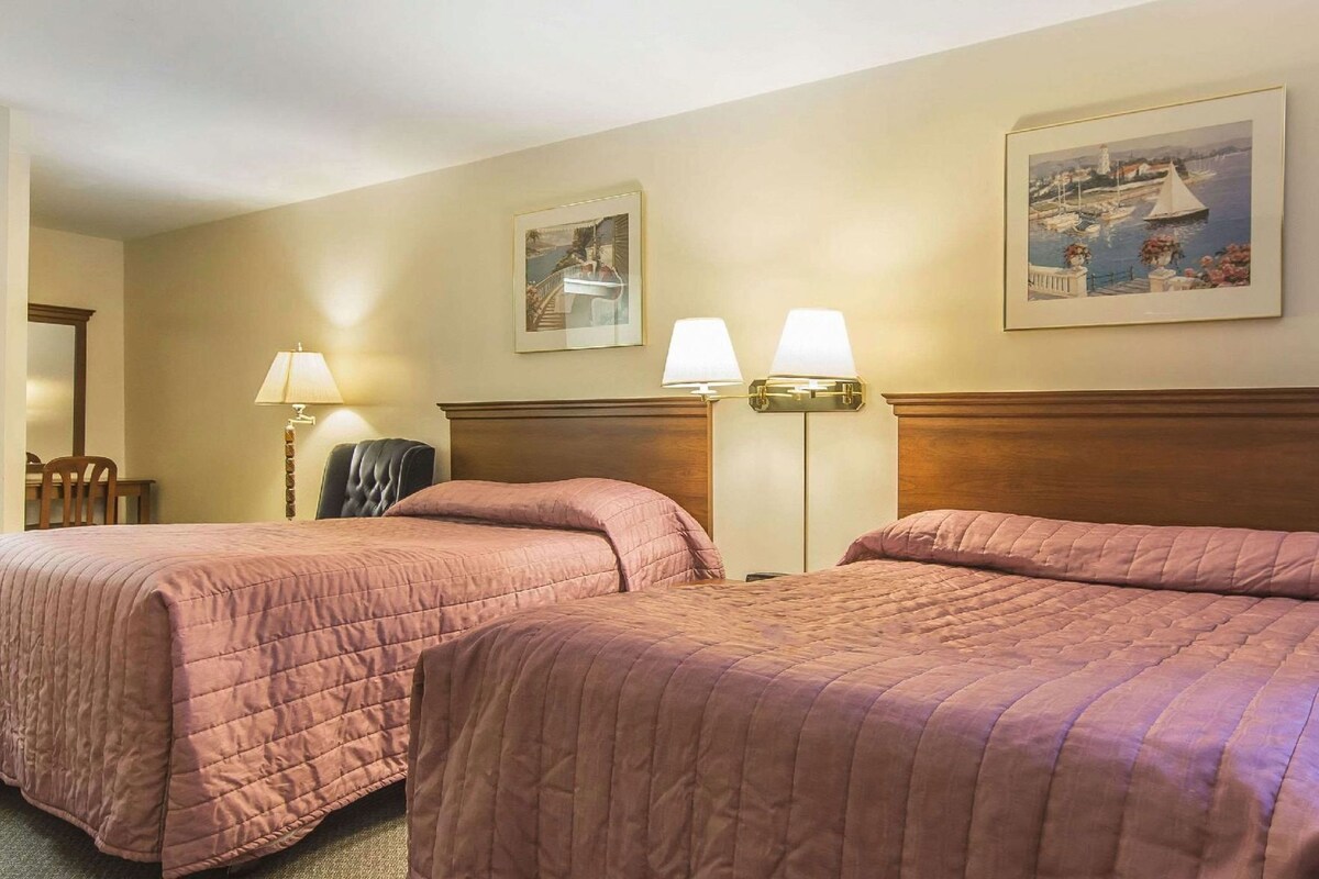 Une chambre d’hôtel avec deux lits, un bureau, une chaise et deux lampes fixées au mur.