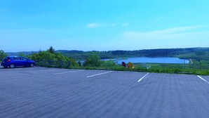Un estacionamiento con un coche azul, una cerca y vistas a un lago y un bosque.