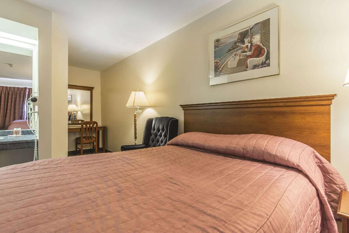 Une chambre d’hôtel avec un lit, un bureau, une chaise, une lampe et un tableau au mur.