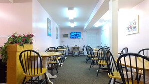 Un comedor con varias mesas y sillas, un televisor montado en la pared y cuadros en las paredes.