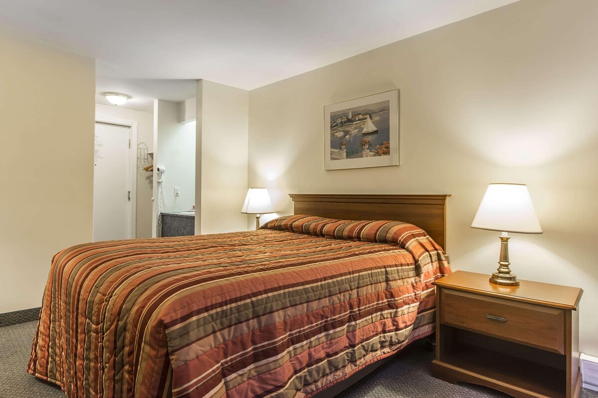 Une chambre d’hôtel avec un grand lit, deux lampes de chevet, une table de nuit en bois et un tableau encadré au mur.
