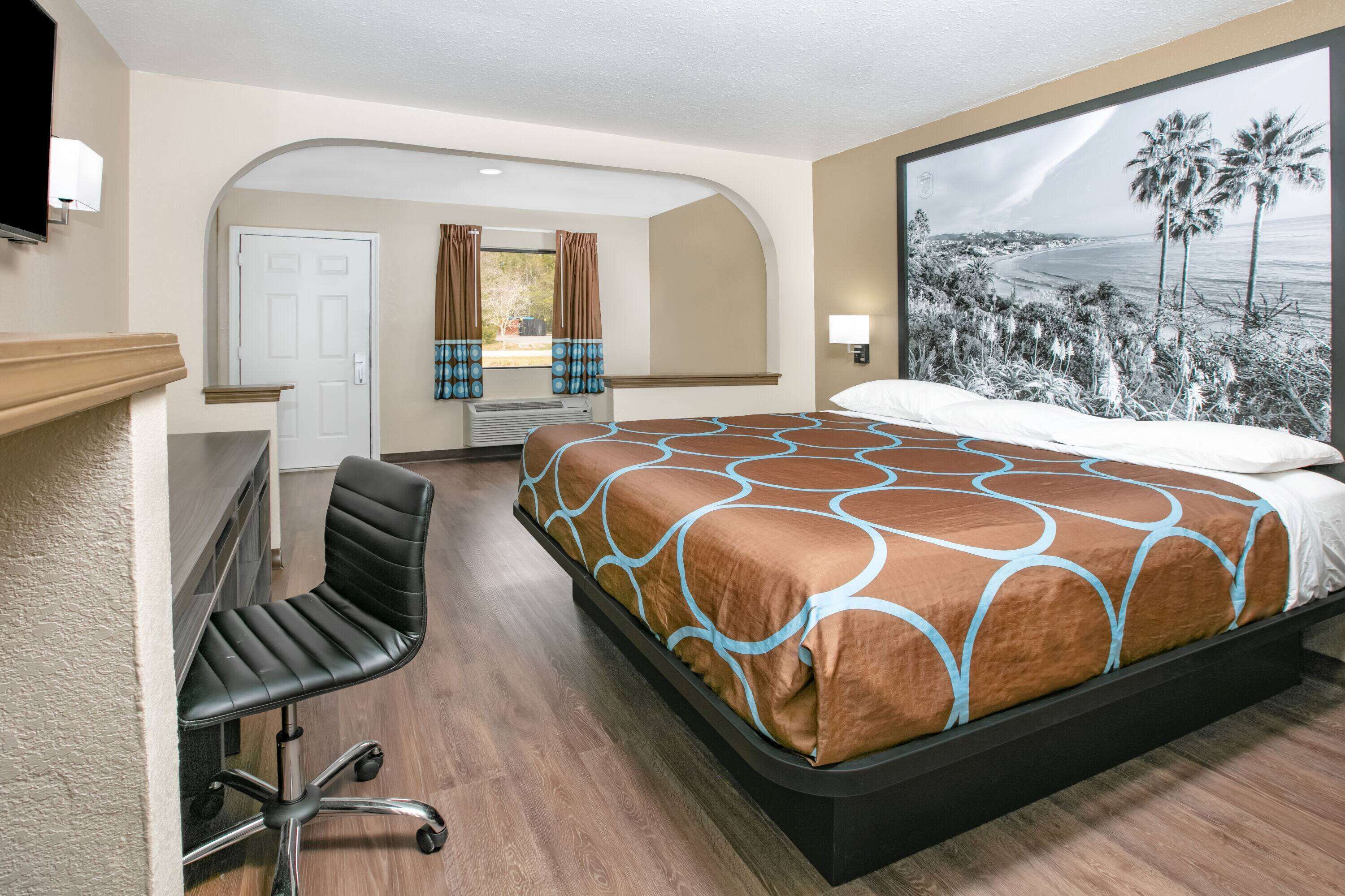 A hotel room with a bed, a desk, and a large window with a beach view.