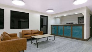 A modern interior with a sofa, a small table, and a kitchen area with a blue backsplash. - Super 8 by Wyndham Moss Point (Moss Point)