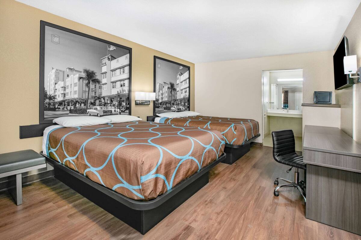 A hotel room with two beds, a desk, a chair, and a TV.