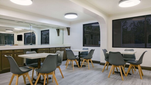 A modern dining area with a rectangular table and six chairs, large windows, and a mirror above the table. - Super 8 by Wyndham Moss Point (Moss Point)
