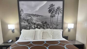 A hotel room with a bed, two bedside lamps, a phone, and a wall-mounted artwork of a beach scene.
