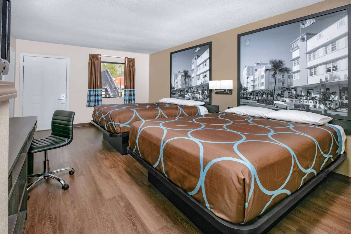 A hotel room with a large bed, a desk, and a chair. There are curtains on the windows and a large picture on the wall.