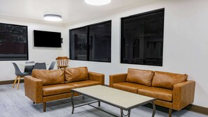 A modern room with two brown leather sofas, a small table, and a TV mounted on the wall. - Super 8 by Wyndham Moss Point (Moss Point)