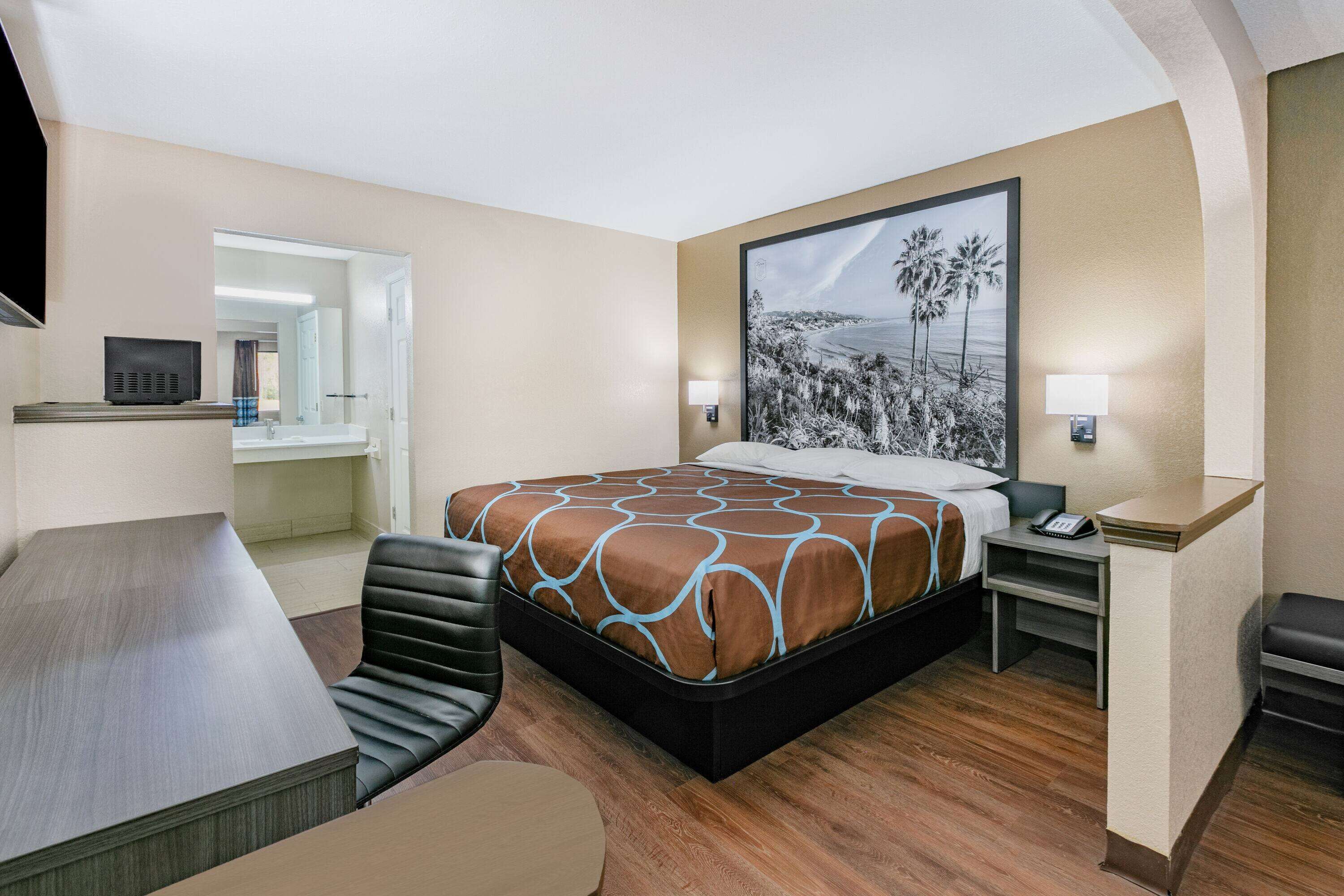 Ein Hotelzimmer mit Bett, Schreibtisch, Stuhl, Nachttisch und einem Bild an der Wand.