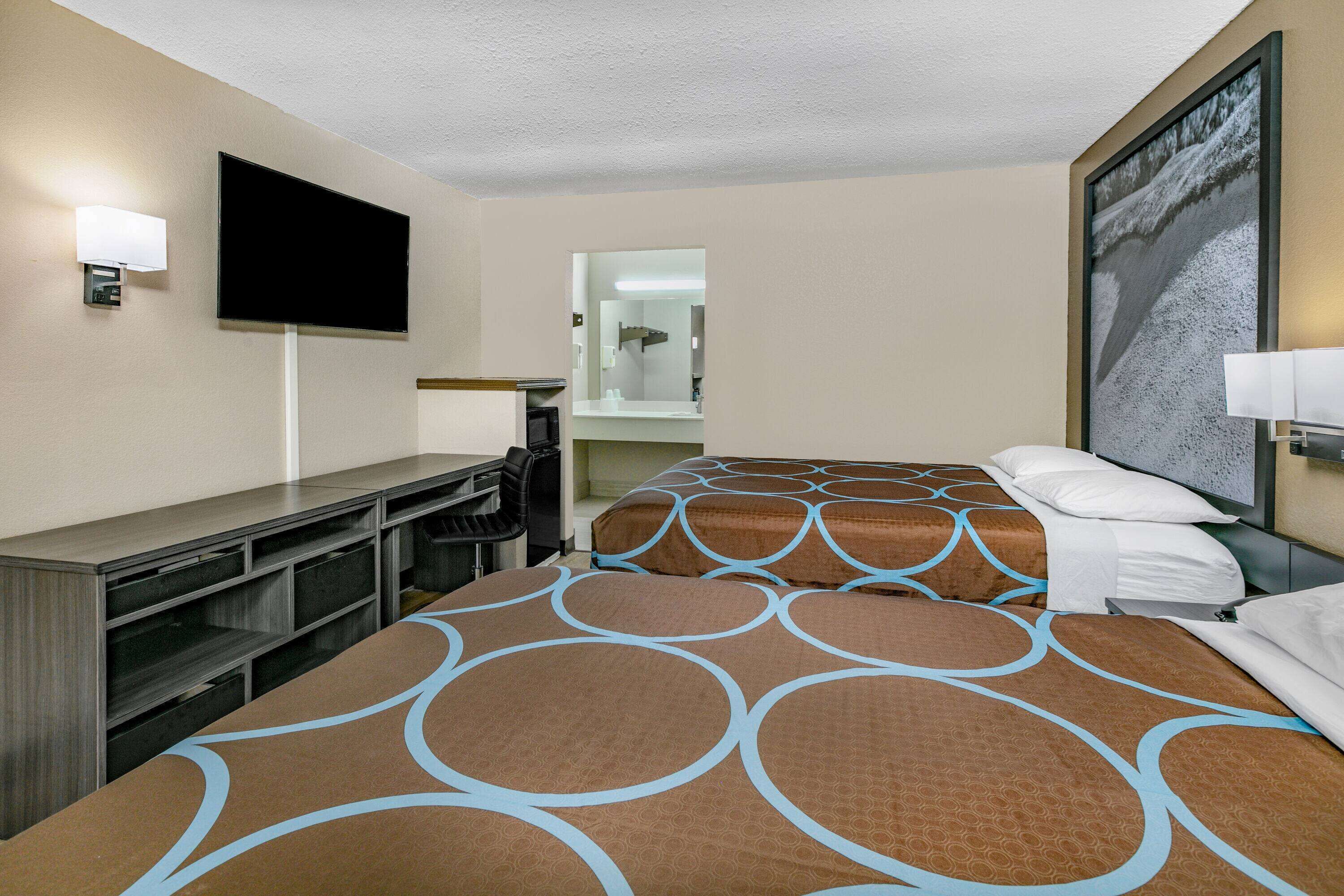 Une chambre d’hôtel avec deux lits, un bureau, un téléviseur à écran plat et un grand tableau au mur.