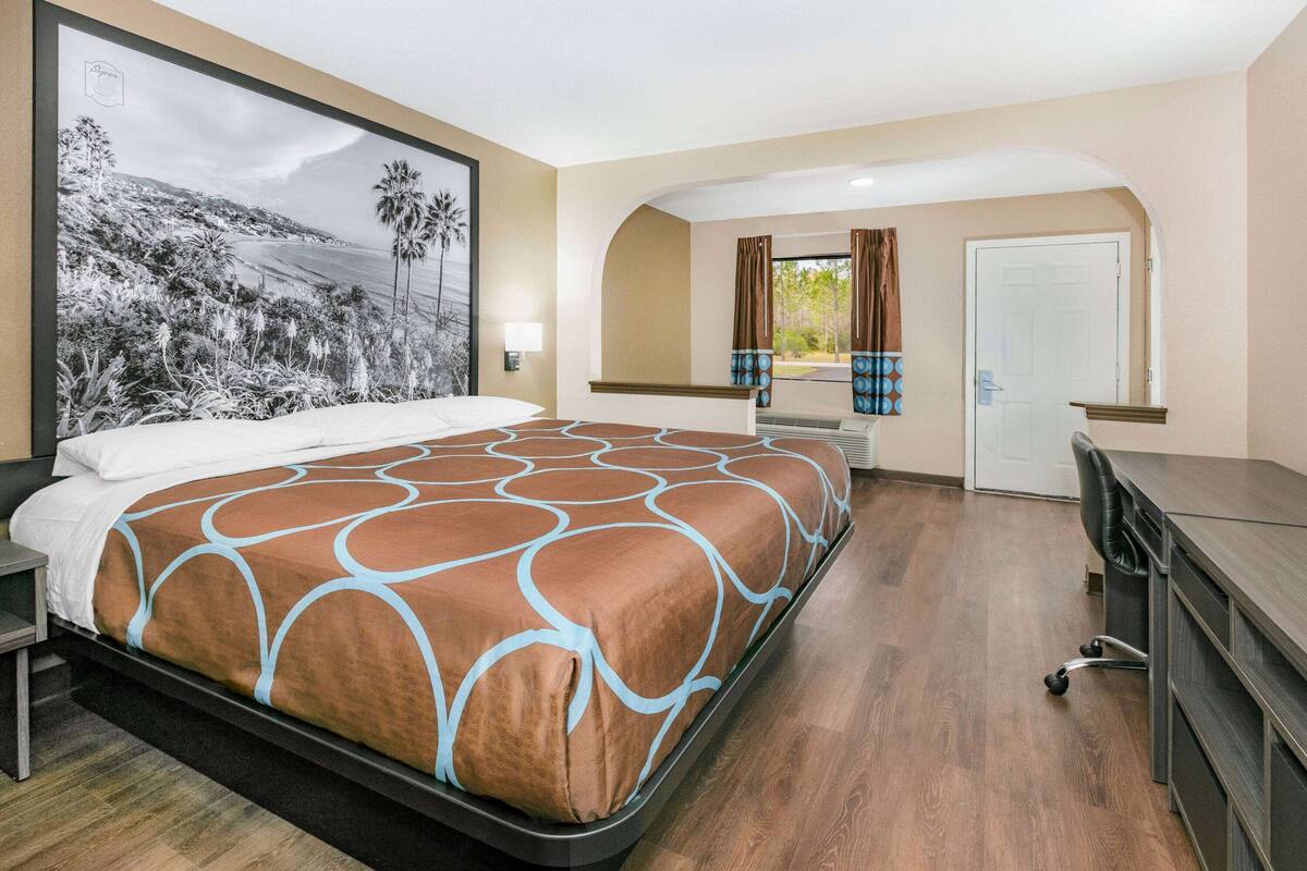 A hotel room with a large bed, a desk, and a view of a landscape painting.