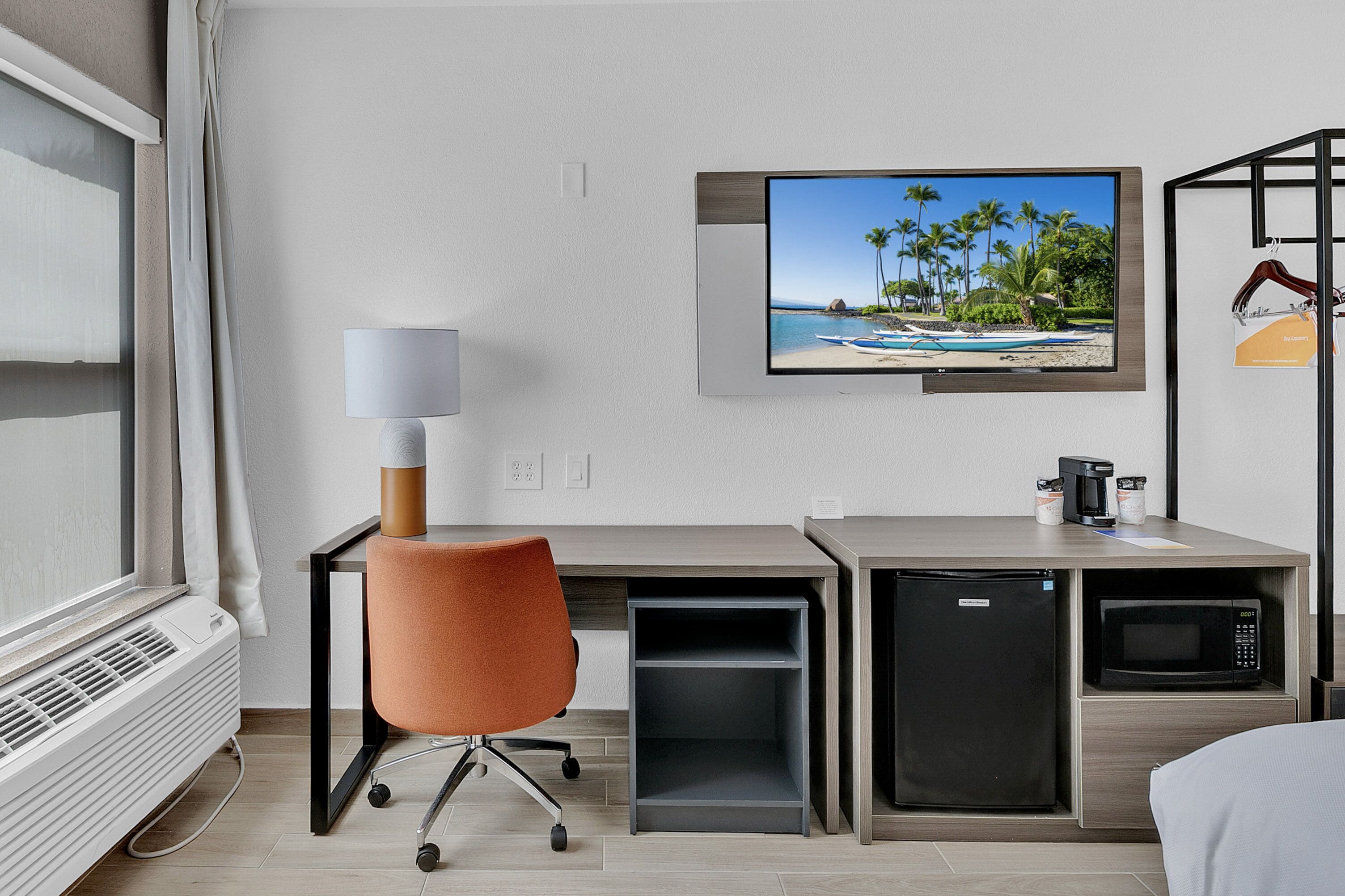 Ein Hotelzimmer mit Schreibtisch, Stuhl, Fernseher, Minikühlschrank, Mikrowelle und Heizung.