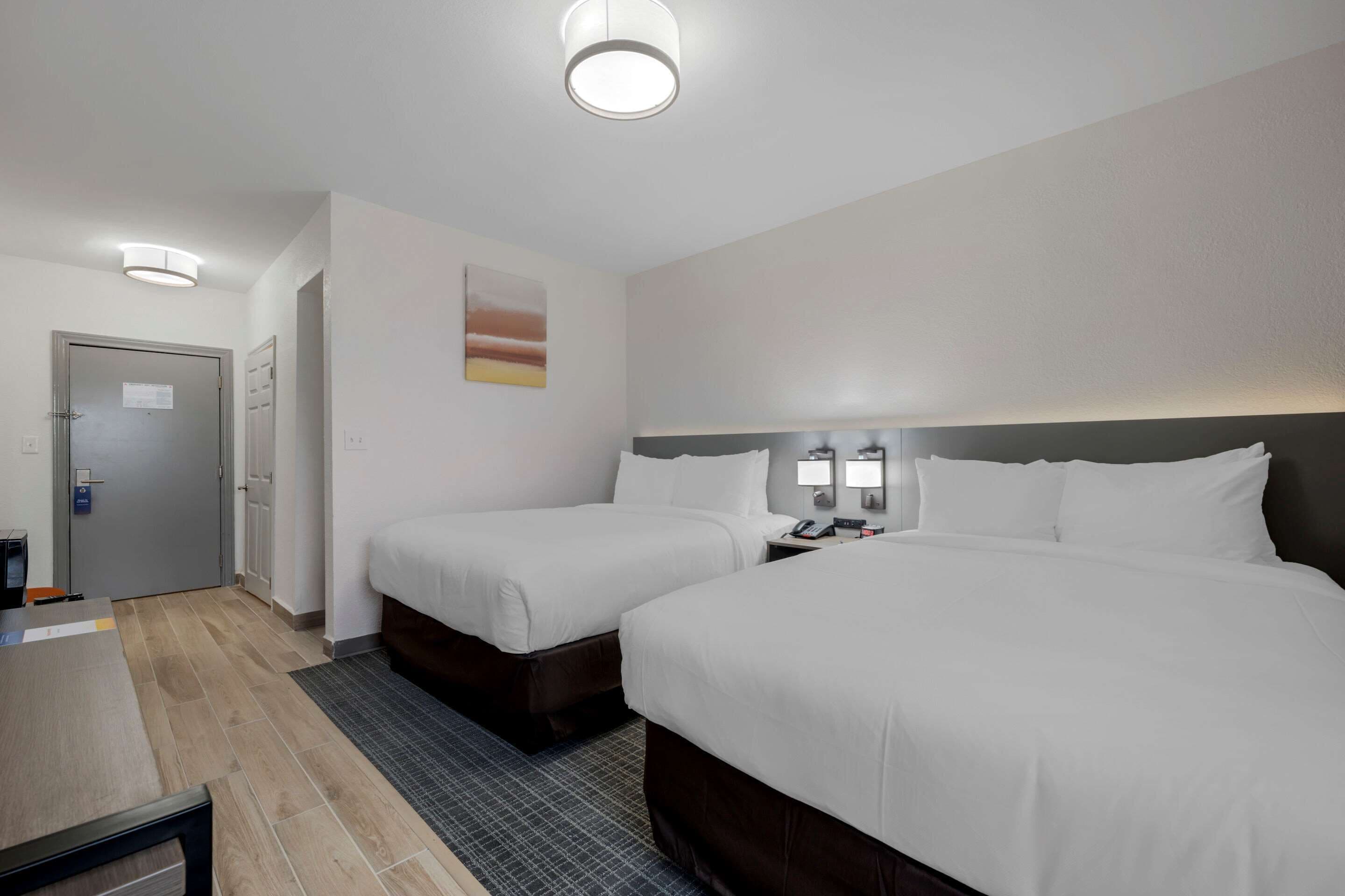 A hotel room with two beds, a desk, a chair, a nightstand, and a wall-mounted lamp.