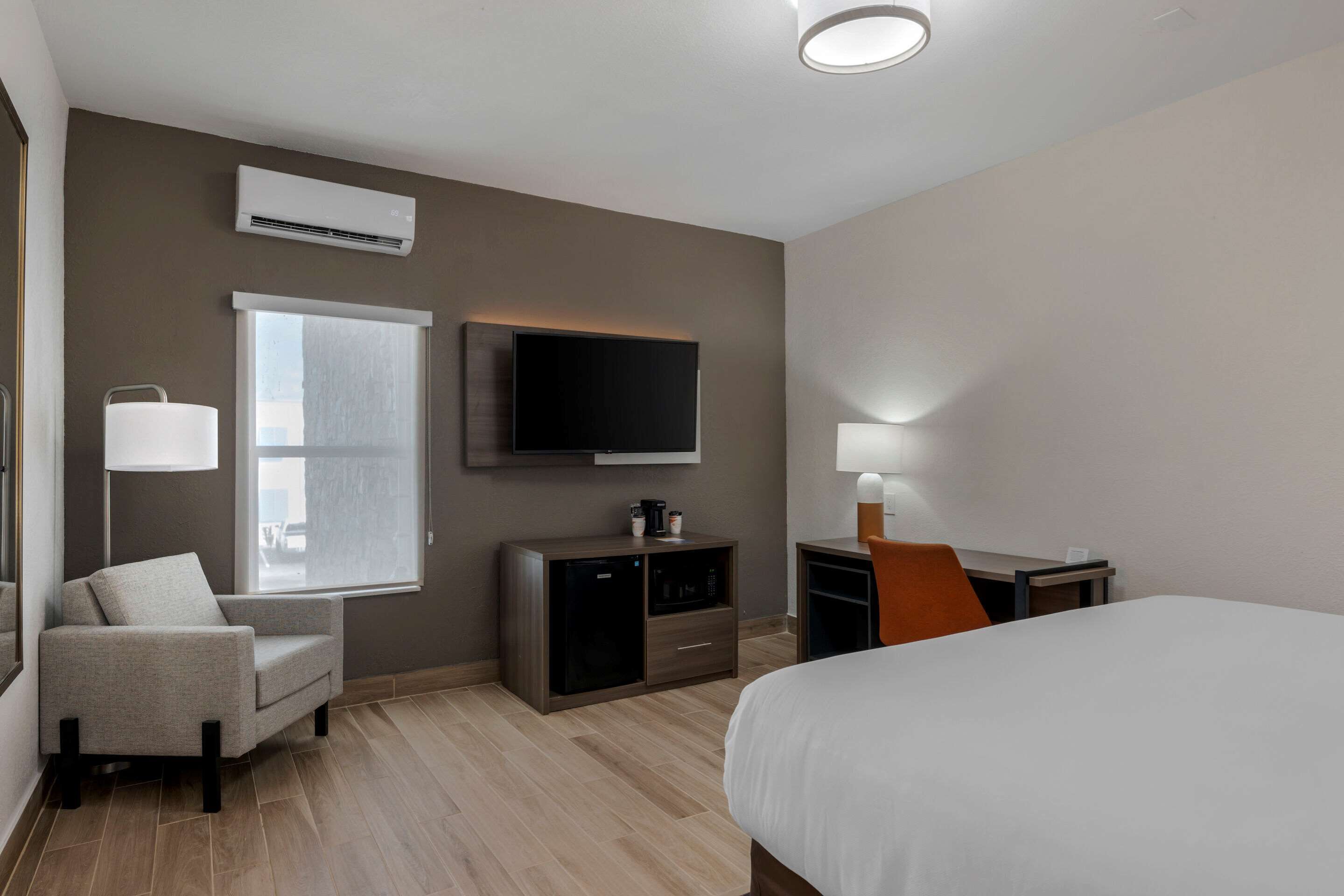 Ein Hotelzimmer mit Bett, Schreibtisch, Sessel, Fernseher, Fenster, Lampe und einer Minibar.
