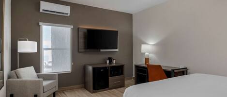 Una habitación de hotel con cama, escritorio, silla, televisor, ventana, lámpara y un minibar.