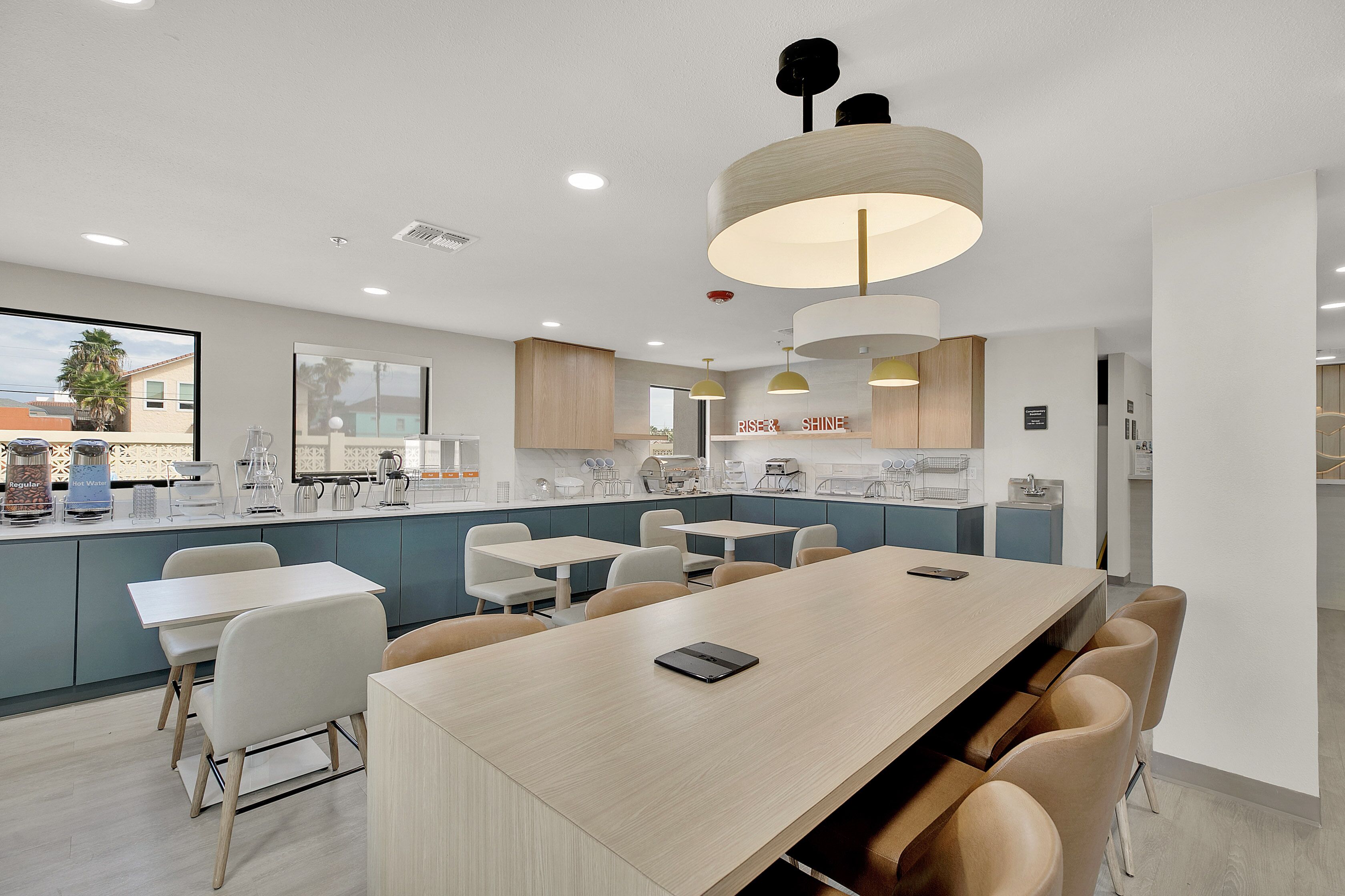Een moderne keuken met een lange eettafel, witte stoelen en uitzicht op buiten.