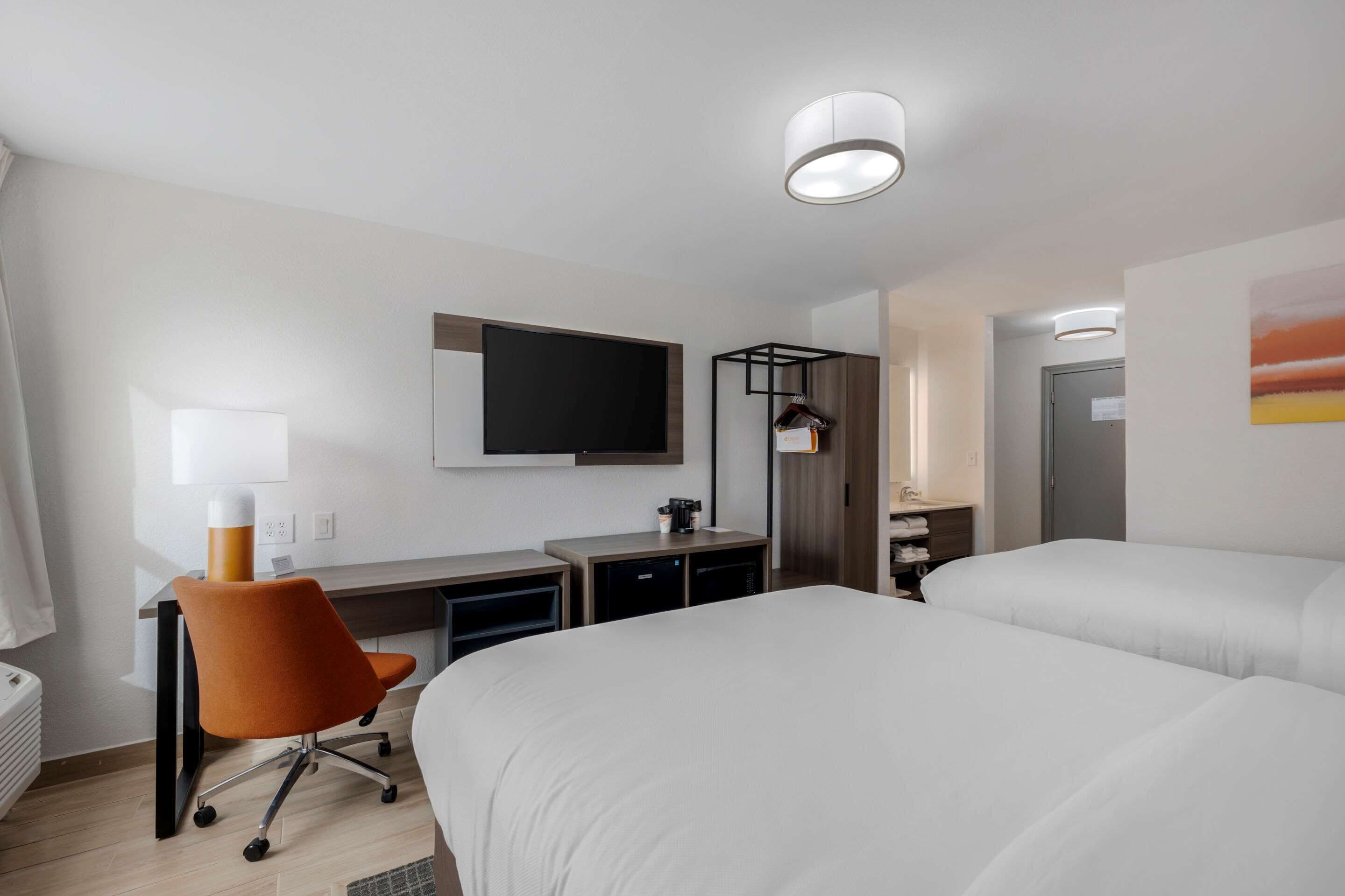 Une chambre d’hôtel avec deux lits, un bureau avec une chaise, un téléviseur fixé au mur et une salle de bain équipée d’un porte-serviettes.