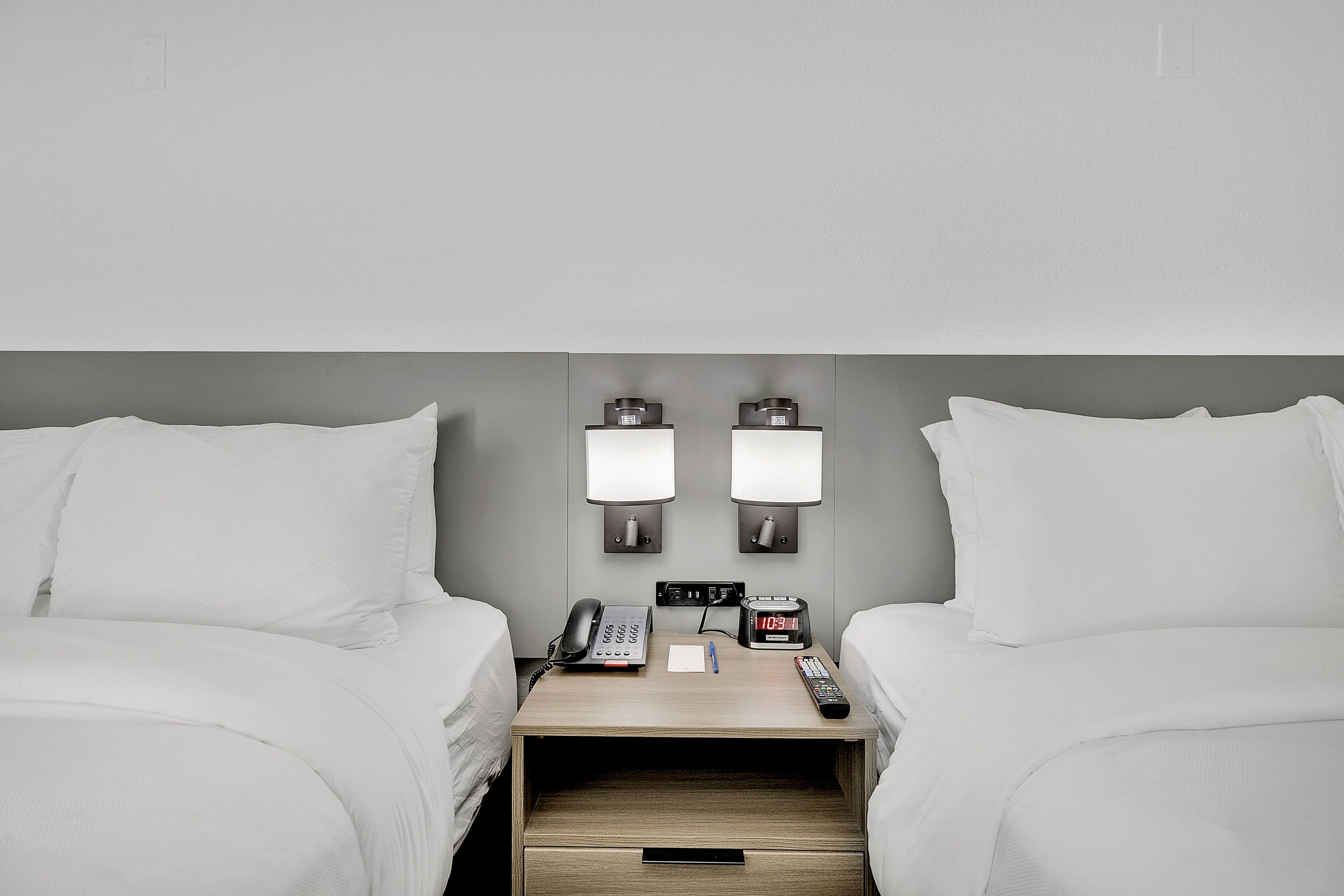 Una habitación de hotel con dos camas, una mesita de noche con un teléfono, un reloj y un control remoto.