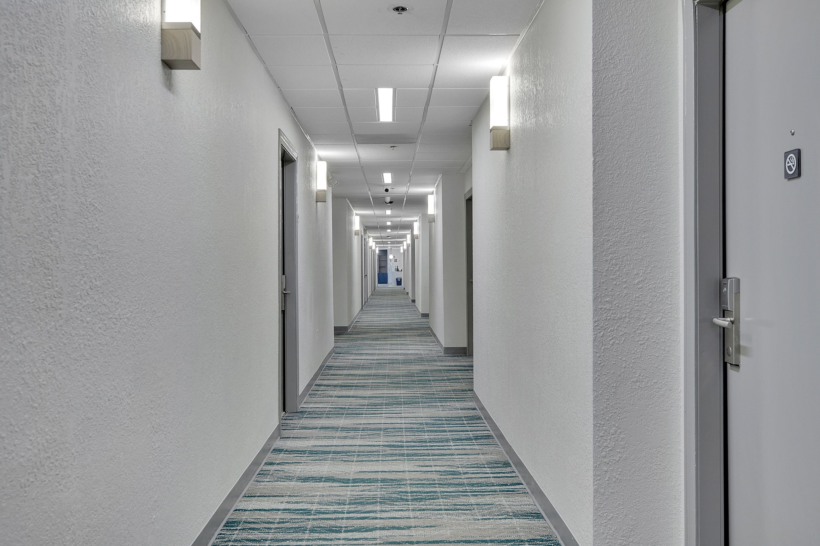 A long, narrow hallway with white walls and a striped carpet.
