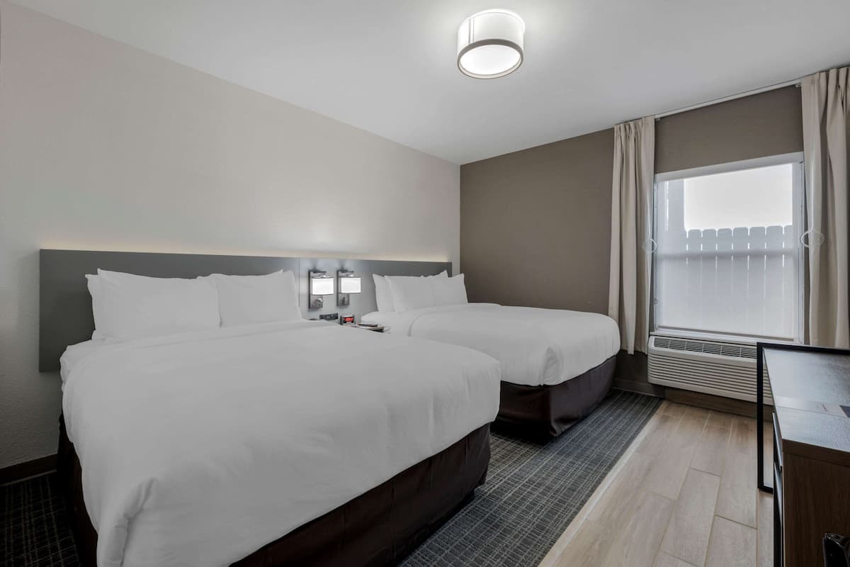 Habitación de hotel con dos camas, un escritorio, una ventana con cortinas y una lámpara en el techo.