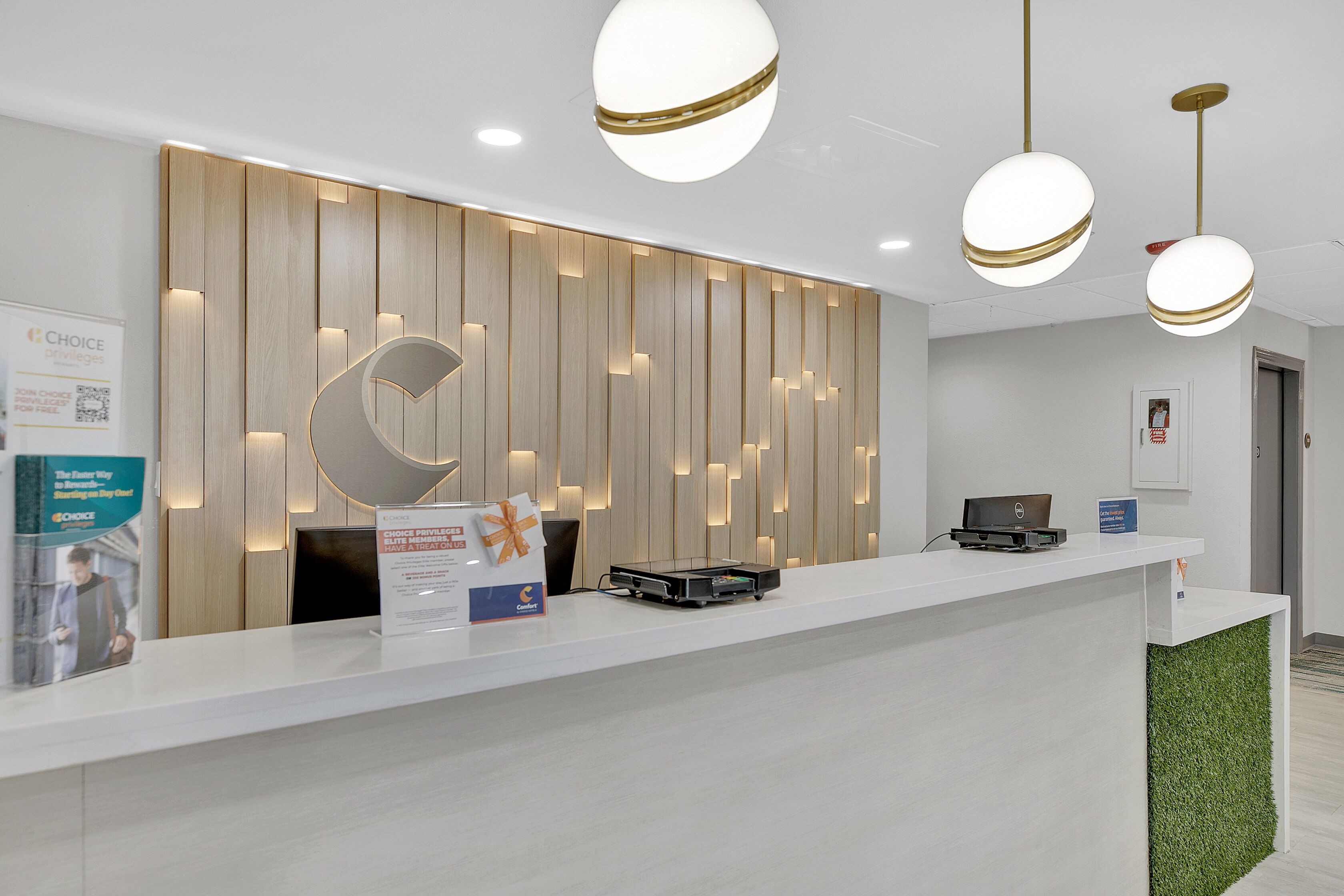 Un mostrador de recepción de diseño moderno, con una encimera blanca, un panel de pared de madera con iluminación integrada y una gran letra 'C' iluminada.