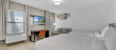 A hotel room with a bed, a desk with a chair, a television, and a window with curtains.
