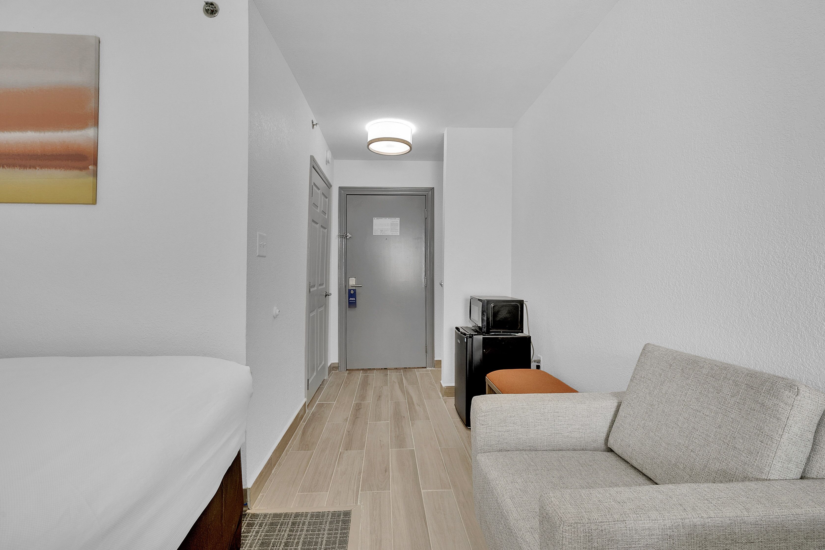 A hotel room with a bed, a sofa, a television, and a door leading to a hallway.