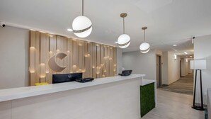 A modern reception desk with a wooden panel wall, two laptops, and a green accent wall.