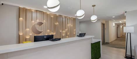 A modern reception desk with a wooden panel wall, two laptops, and a green accent wall.