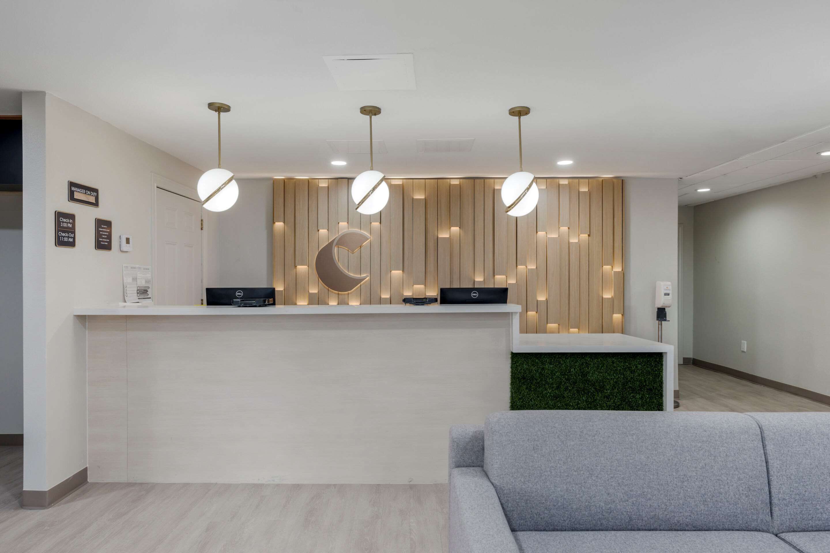 Un área de recepción moderna con un mostrador blanco, un sofá gris y luminarias colgantes.