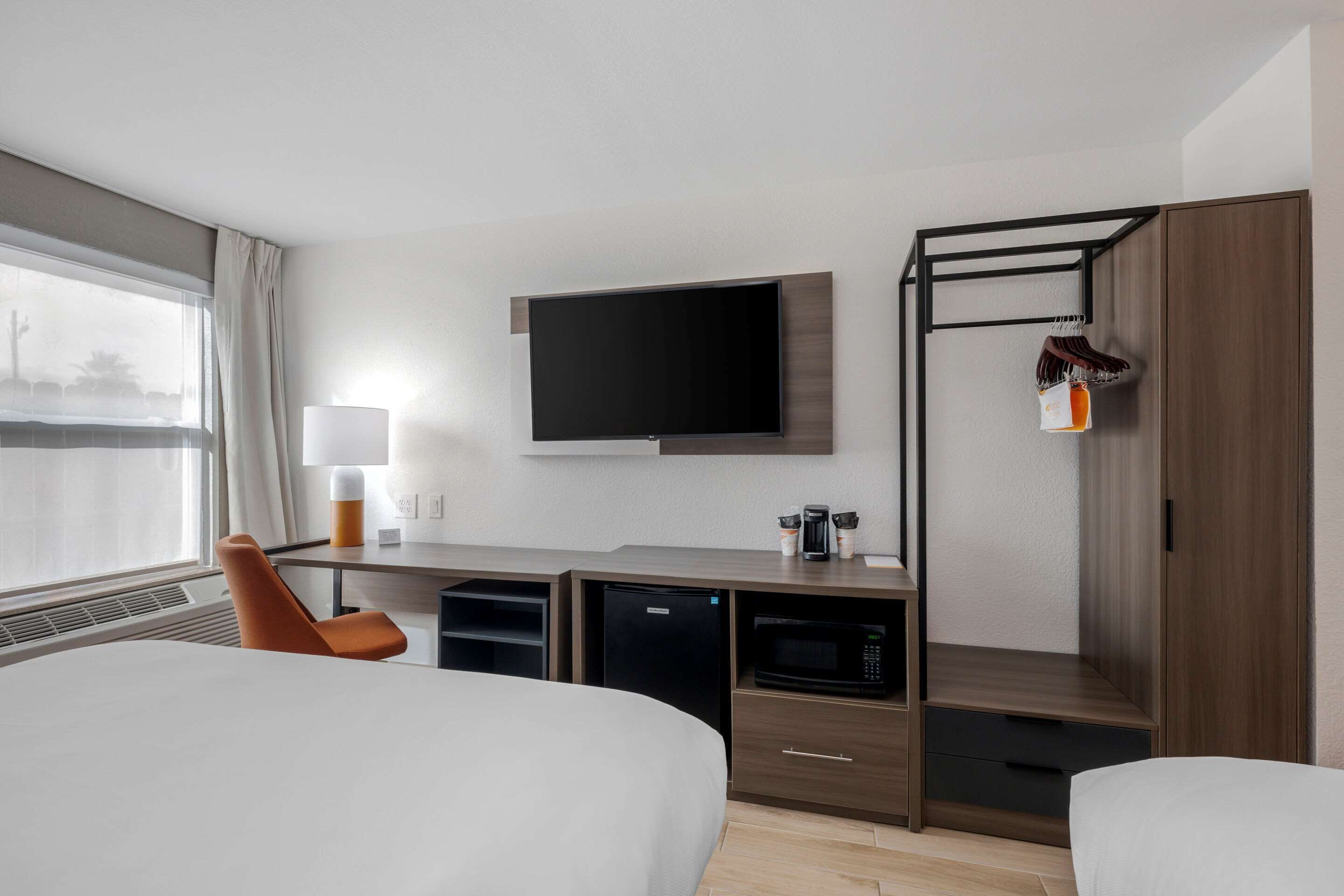 Una habitación de hotel con cama, escritorio, televisor de pantalla plana, microondas y refrigerador pequeño.