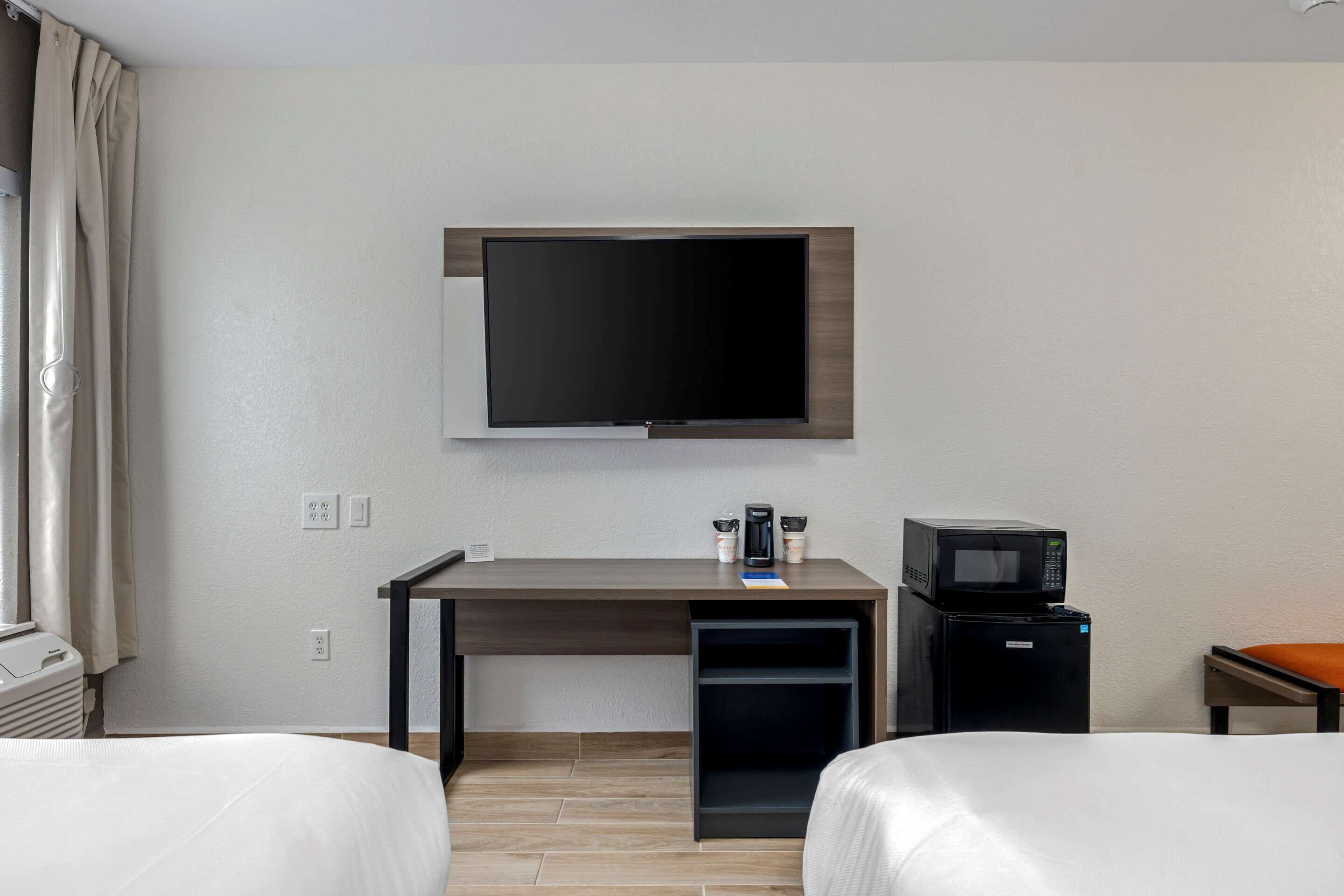 Quarto de hotel com cama, escrivaninha, televisão de tela plana, cafeteira, micro-ondas e mini-geladeira.