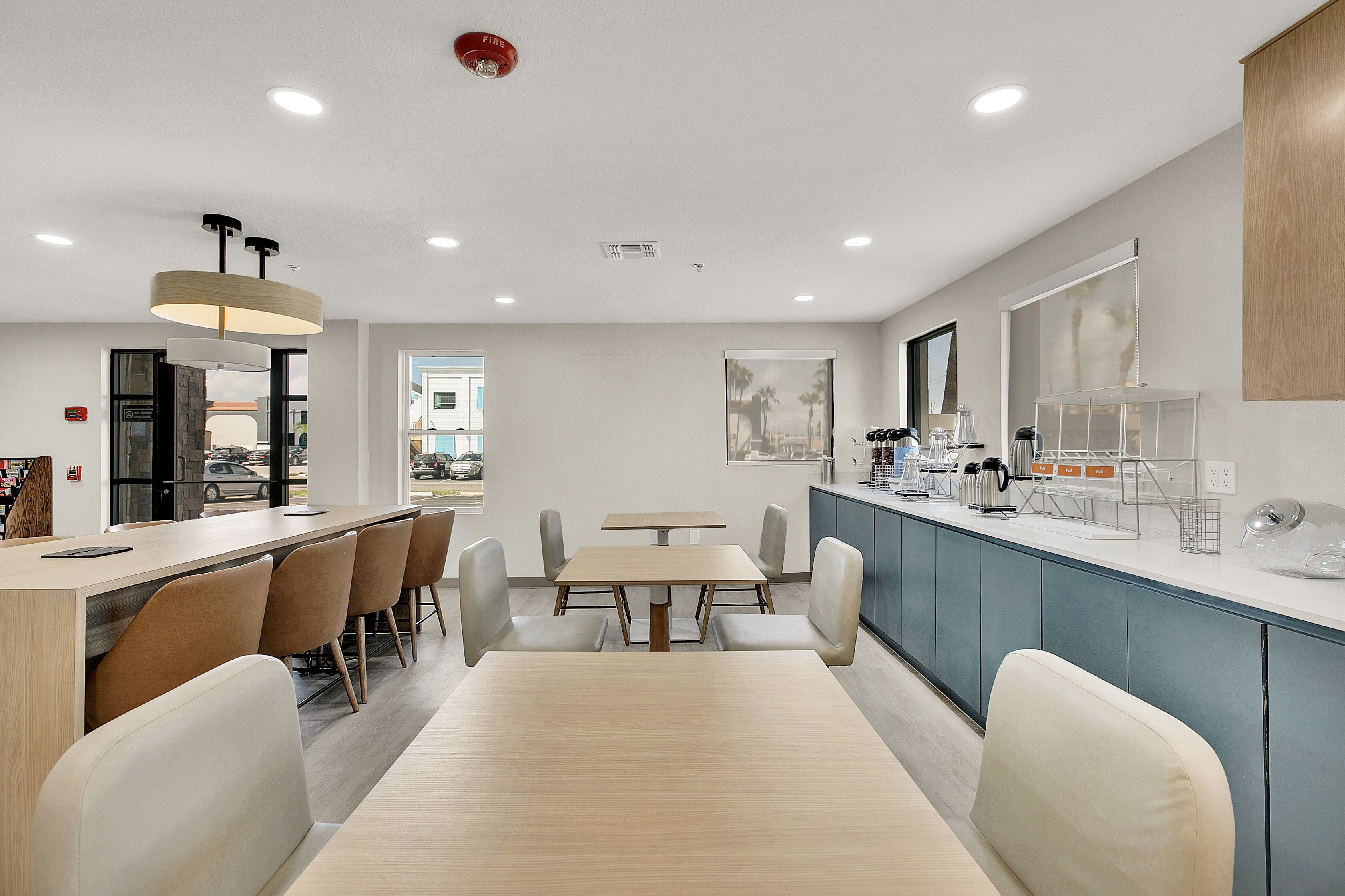 Un área de comedor moderna con una larga mesa y sillas, una barra con máquinas de café y vistas al exterior.