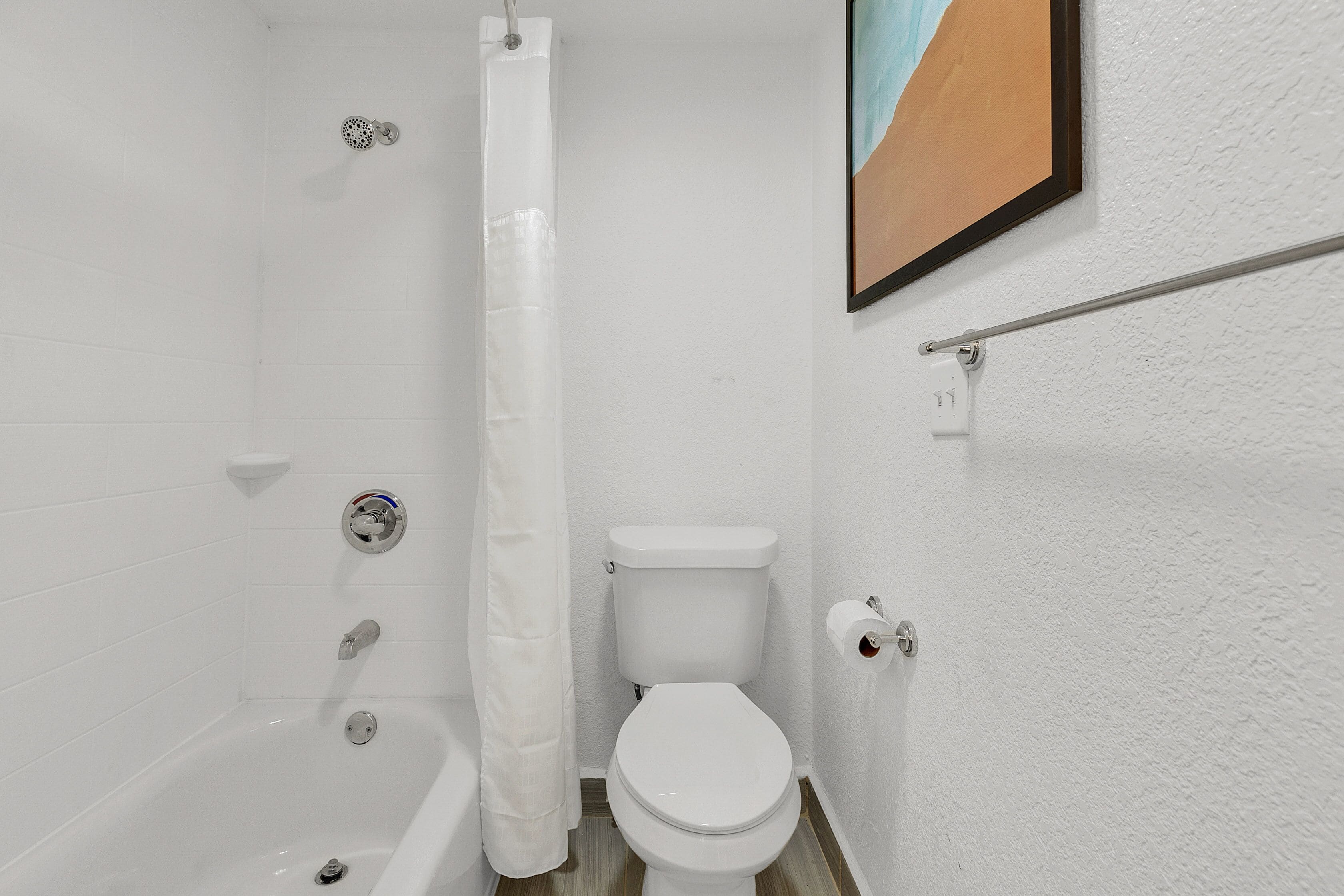 A bathroom with a white toilet, a shower with a curtain, and a towel rack.
