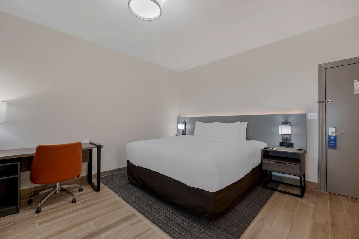 Una habitación de hotel con una cama, un escritorio con una silla, una mesita de noche y una puerta.