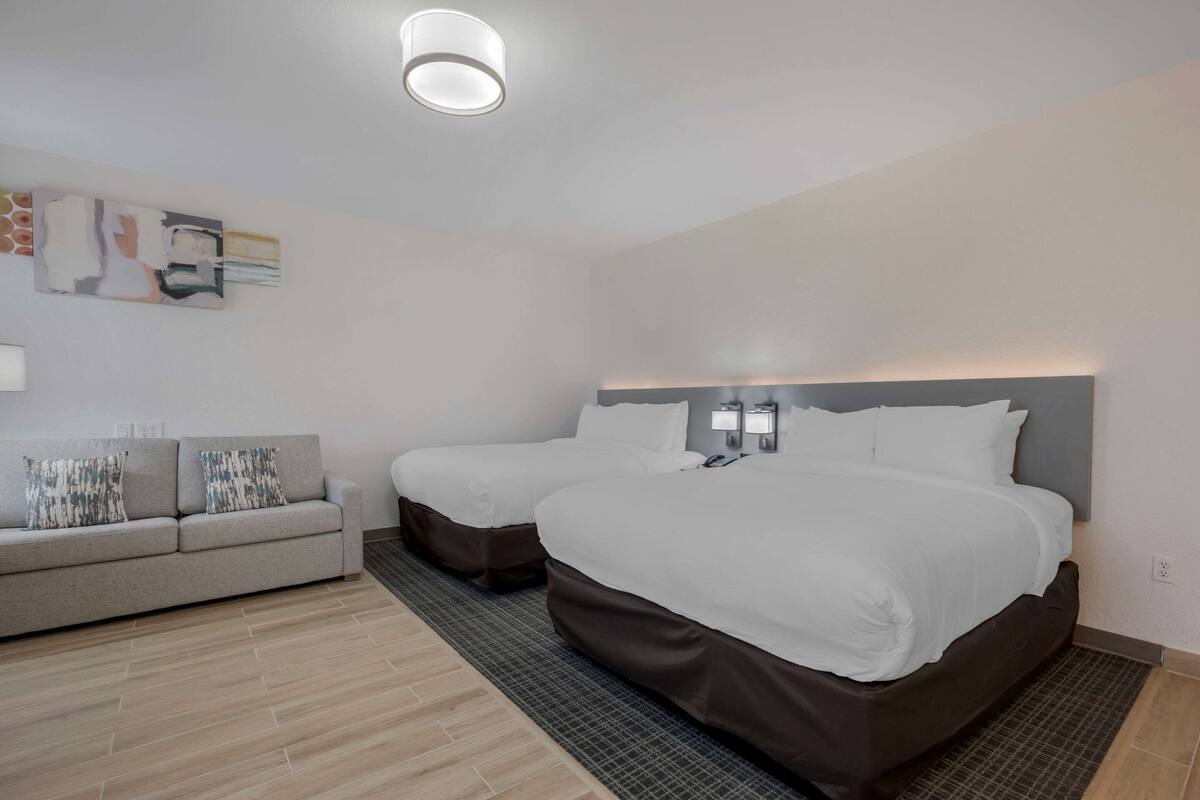 Habitación de hotel con dos camas, un sofá y una obra de arte colgada en la pared.
