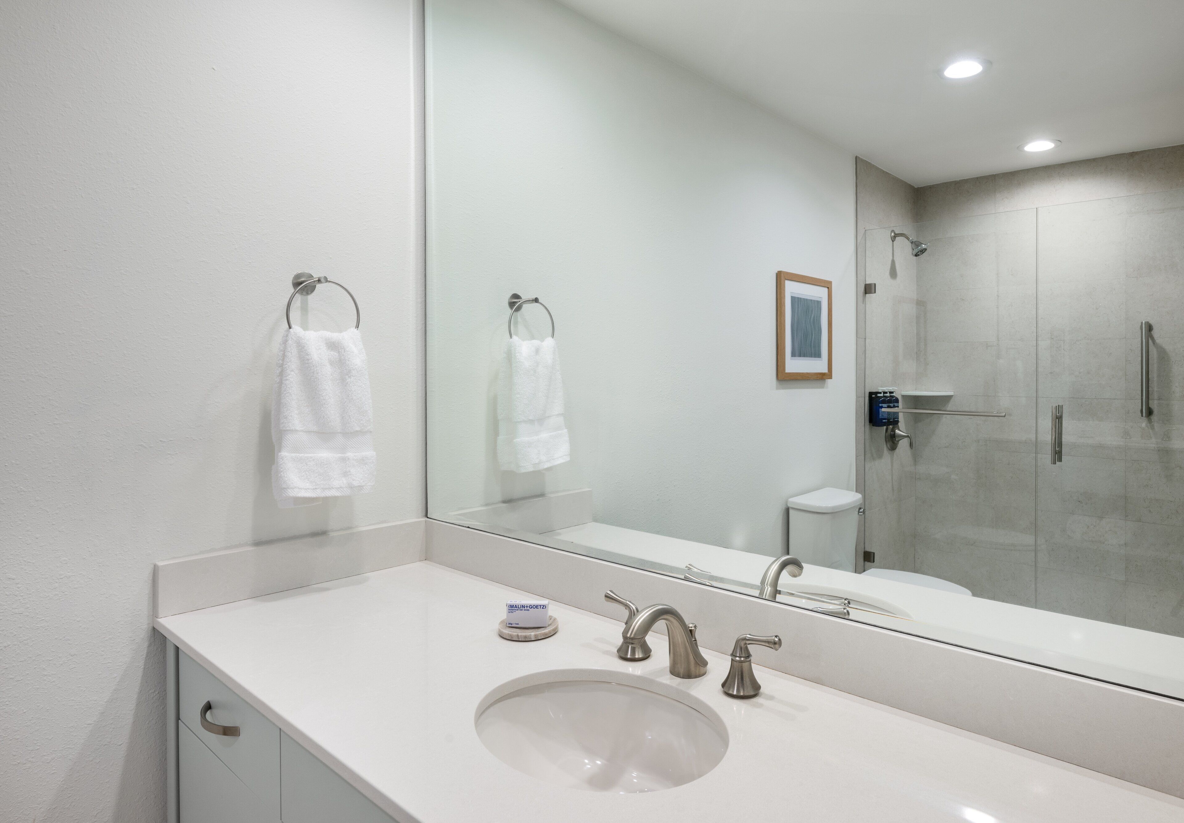 A modern bathroom with a large mirror, a sink, two faucets, and a shower area.