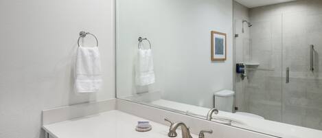 A modern bathroom with a large mirror, a sink, two faucets, and a shower area.