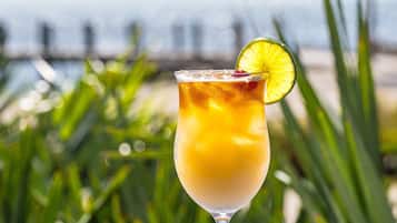 A cocktail glass with a lime garnish on a blue table, set against a beach backdrop with palm trees and ocean view.