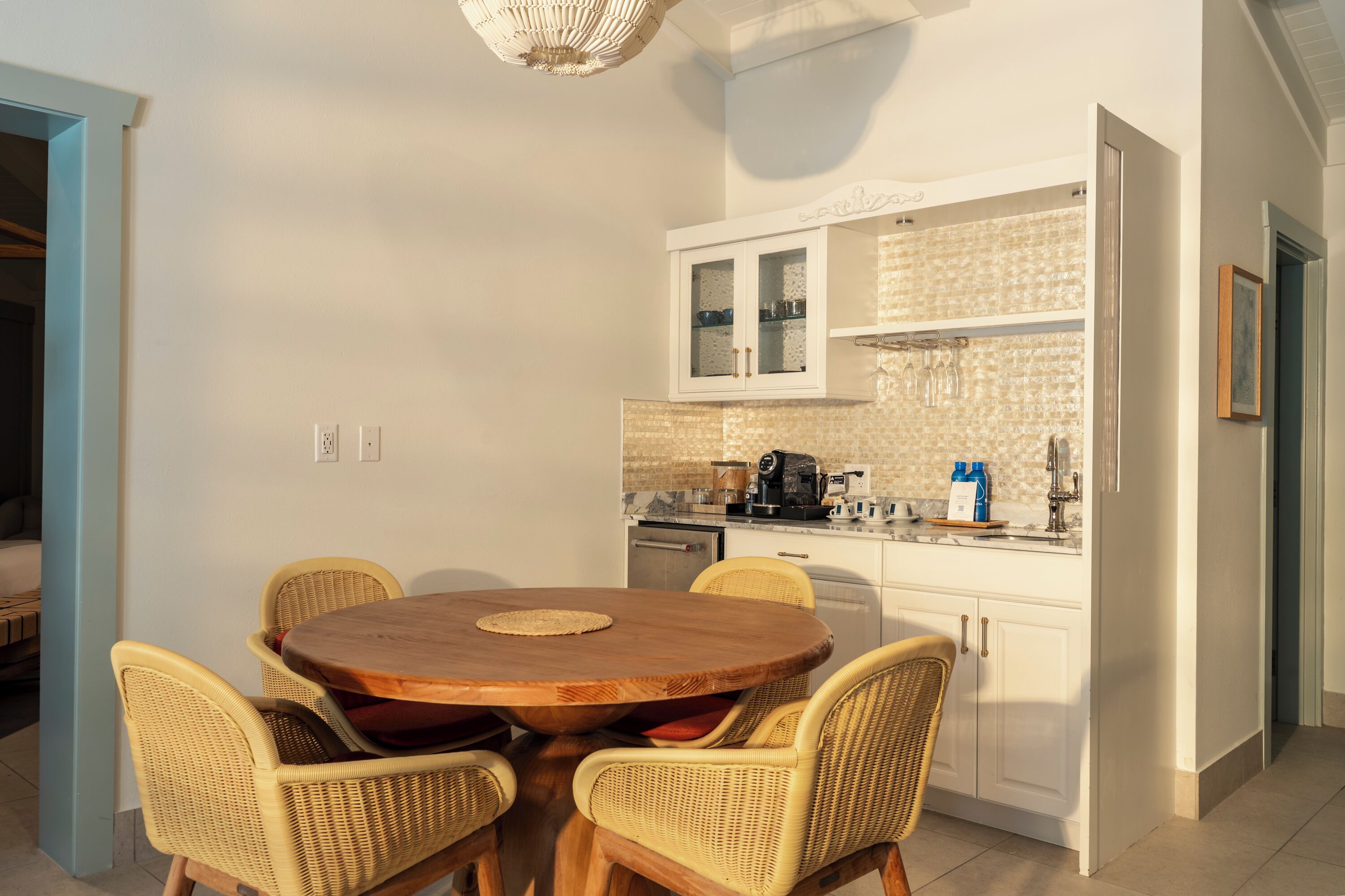 Una cocina compacta con muebles blancos, una mesa redonda de madera y sillas de mimbre.