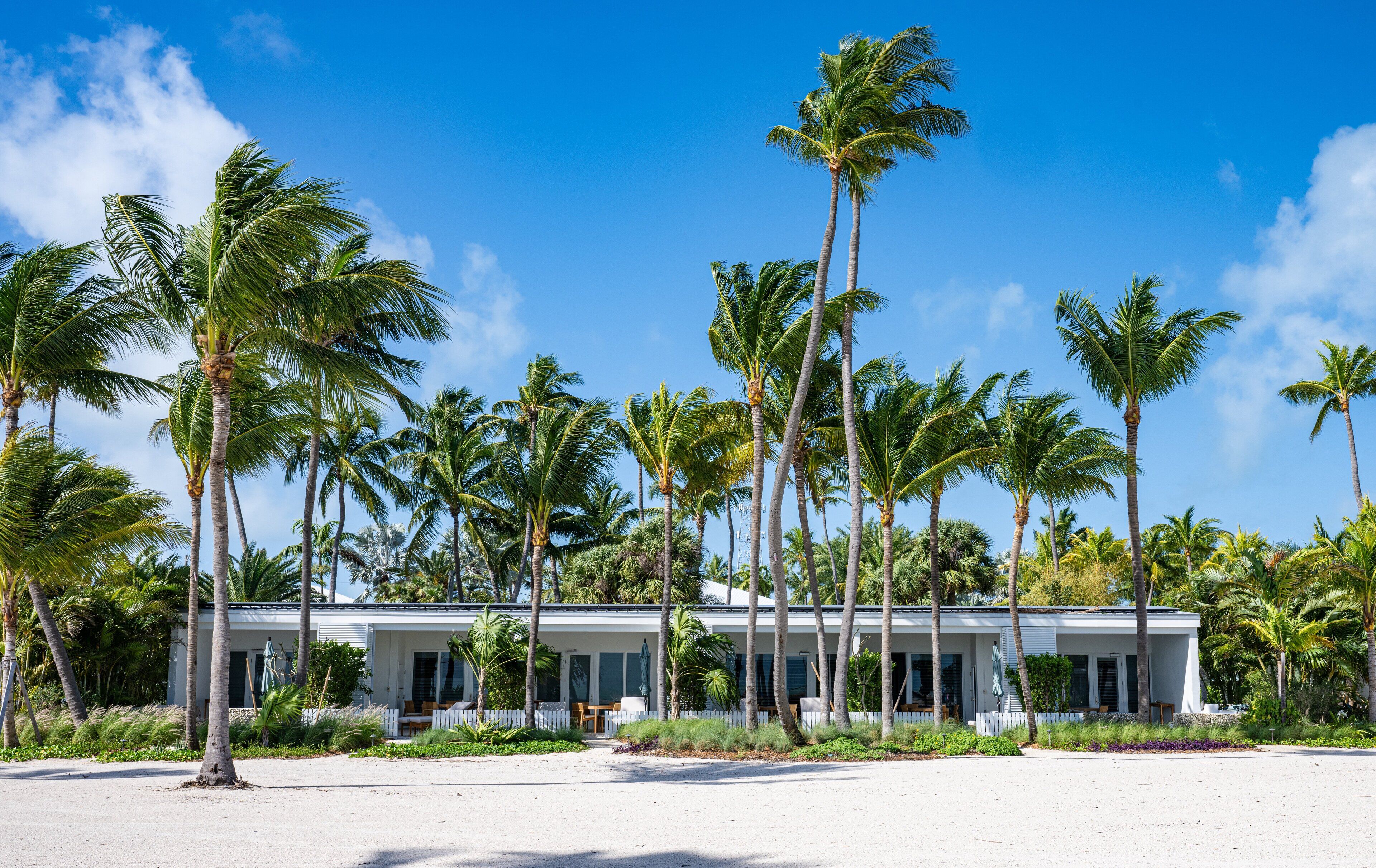 A beachfront hotel with a white exterior, multiple rooms, and a sandy beach in front.