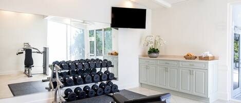 A home gym with exercise equipment, a television, and a kitchen area.