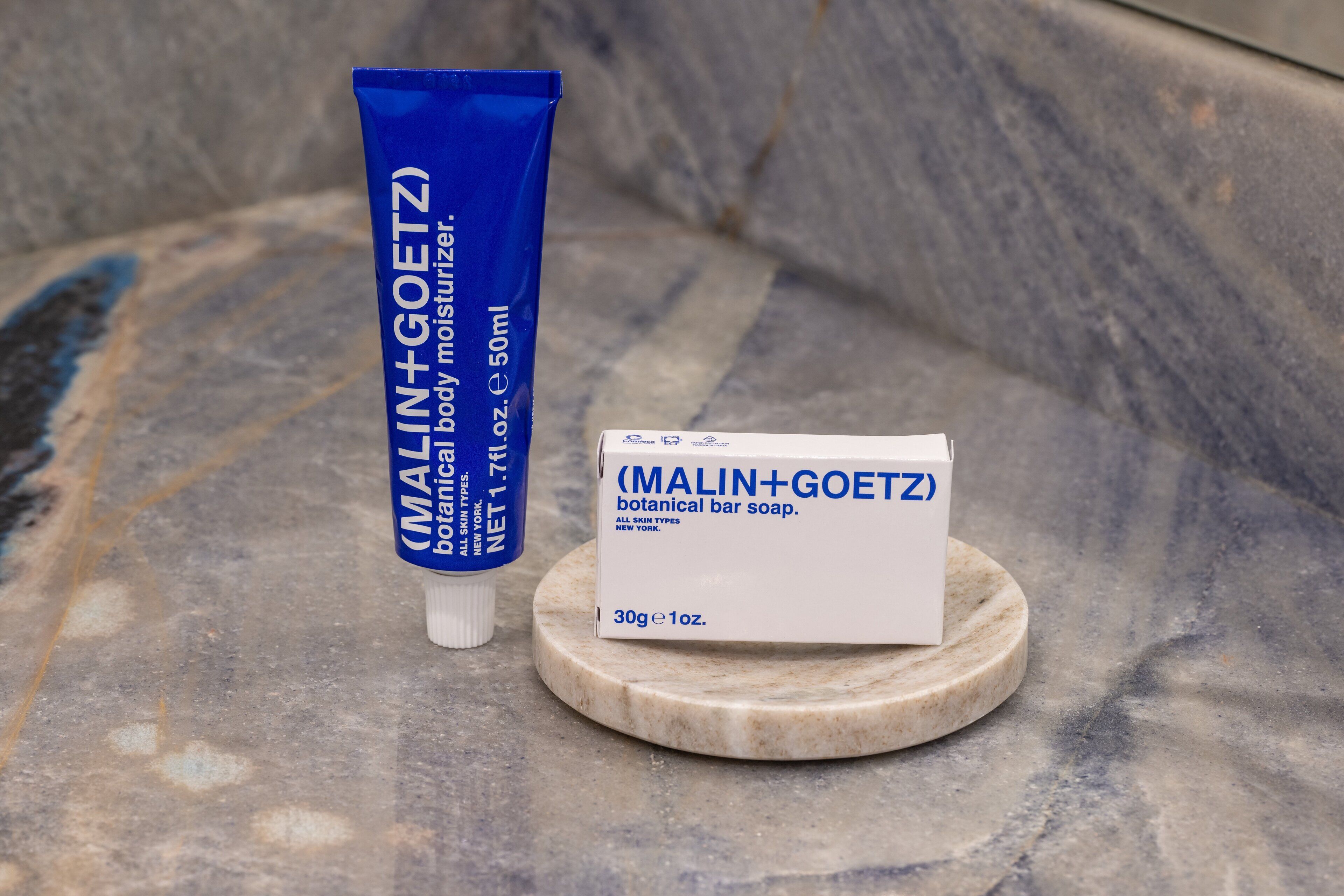 Eine blaue Tube und Verpackung der MALIN+GOETZ Botanical Bar Seife auf einer Marmorplatte.