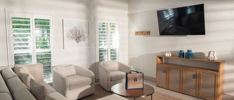A modern living room with a sofa, armchairs, a coffee table, and a TV mounted on the wall.